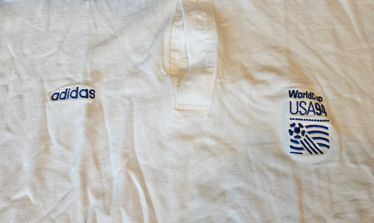 Close-up of embroidered Adidas wordmark and official FIFA World Cup USA 94 logo on white polo shirt
